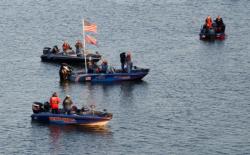 Anglers, including those in the National Guard-wrapped tourney boat, stand at attention for the singing of the national anthem before takeoff on day two.